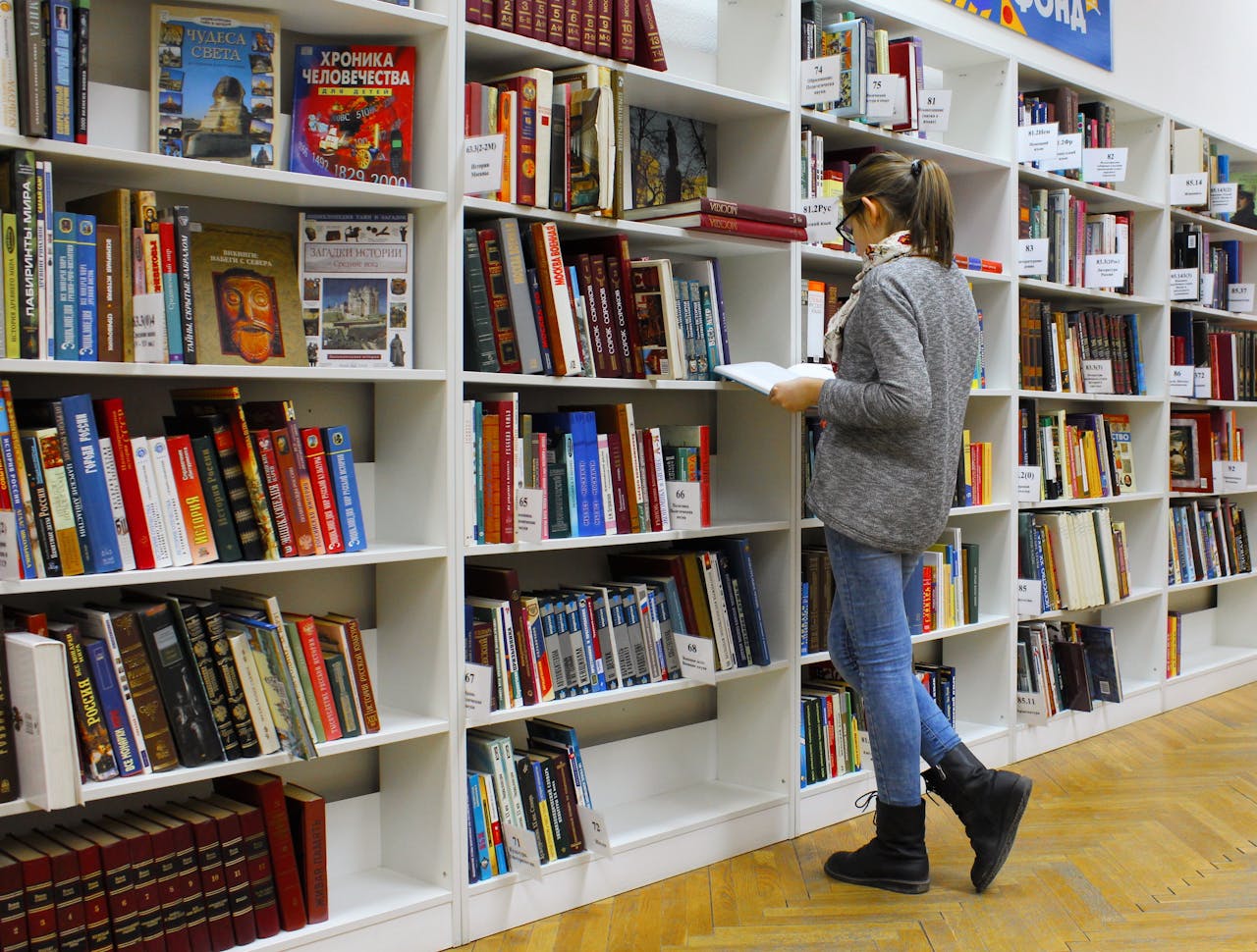 services-01 A young woman stands reading a book in a well-stocked library.