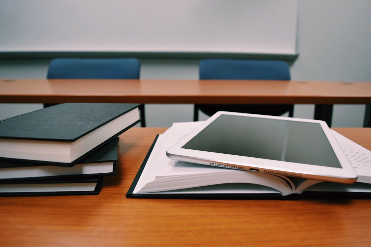 services-02 Books and a tablet on a desk in a classroom, depicting modern education.